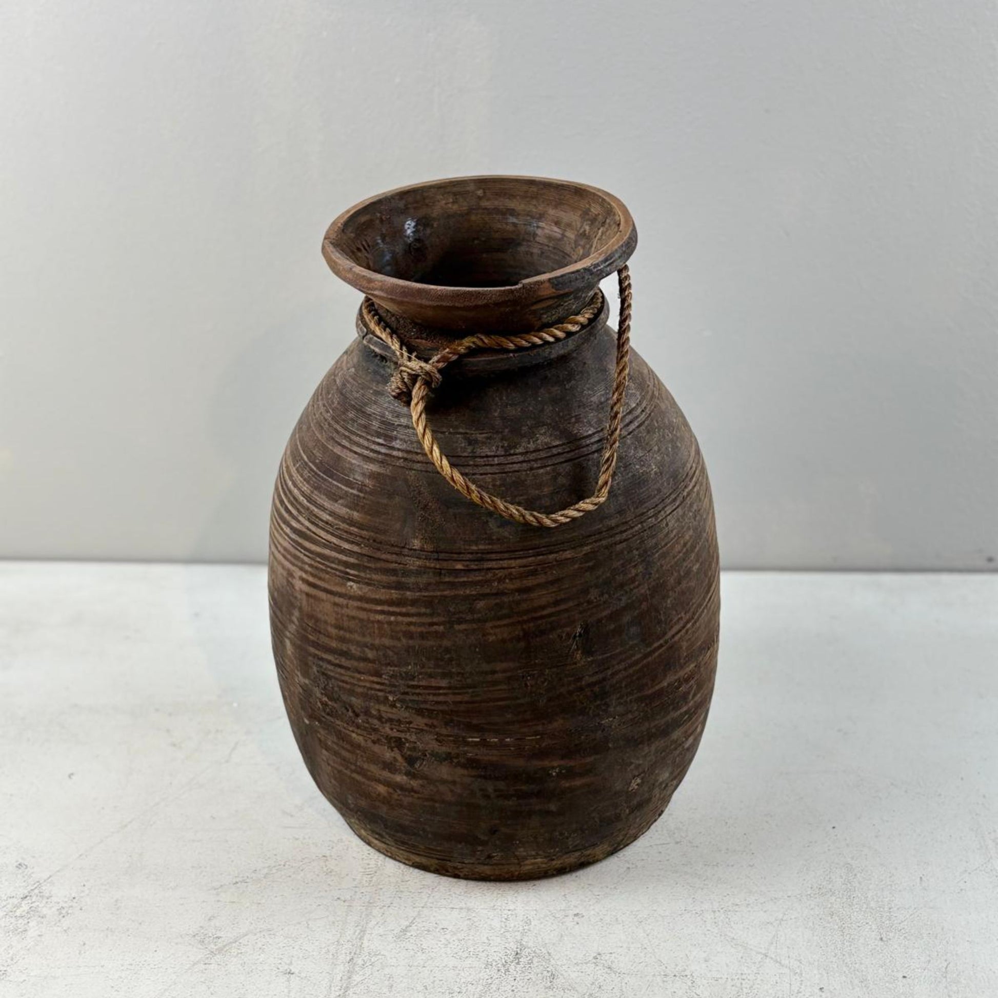 Brown ceramic vase with rope handle on a white surface and light gray background
